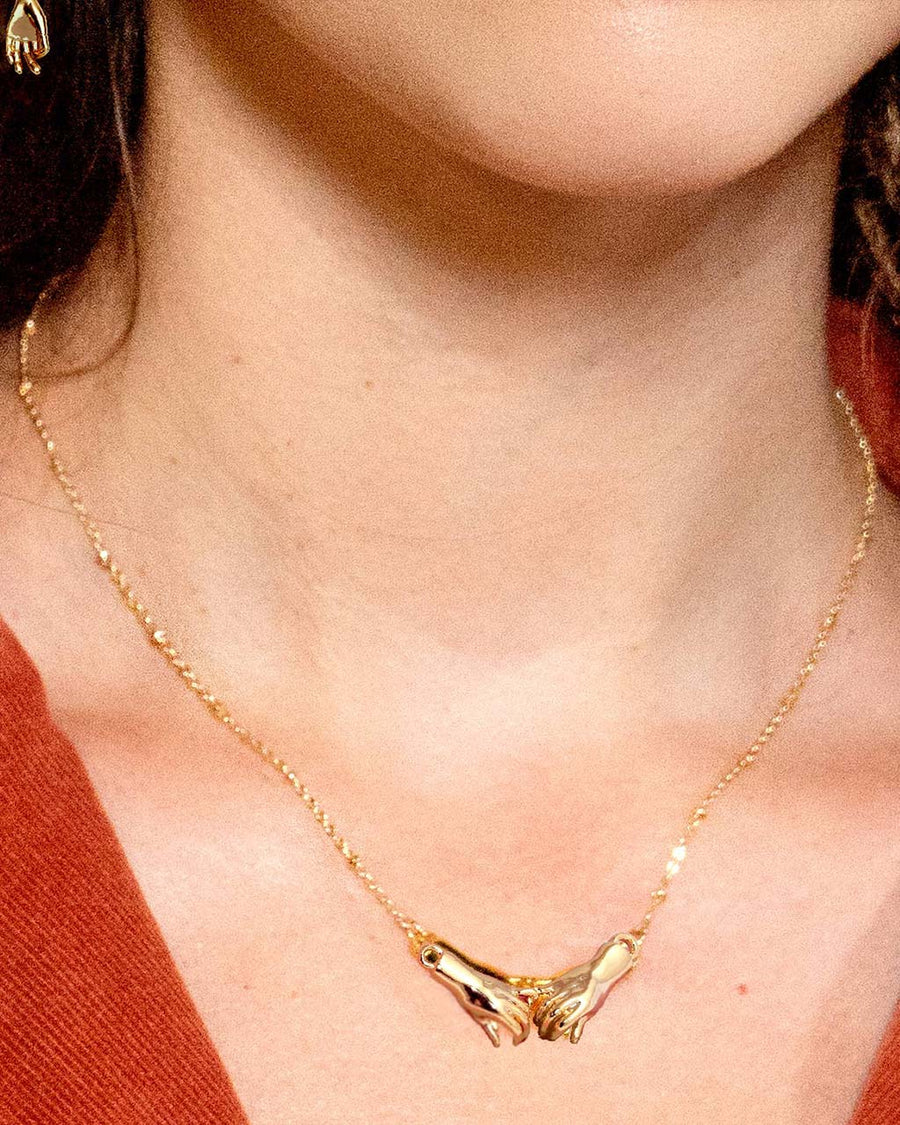up close of model wearing gold necklace with two holding hands