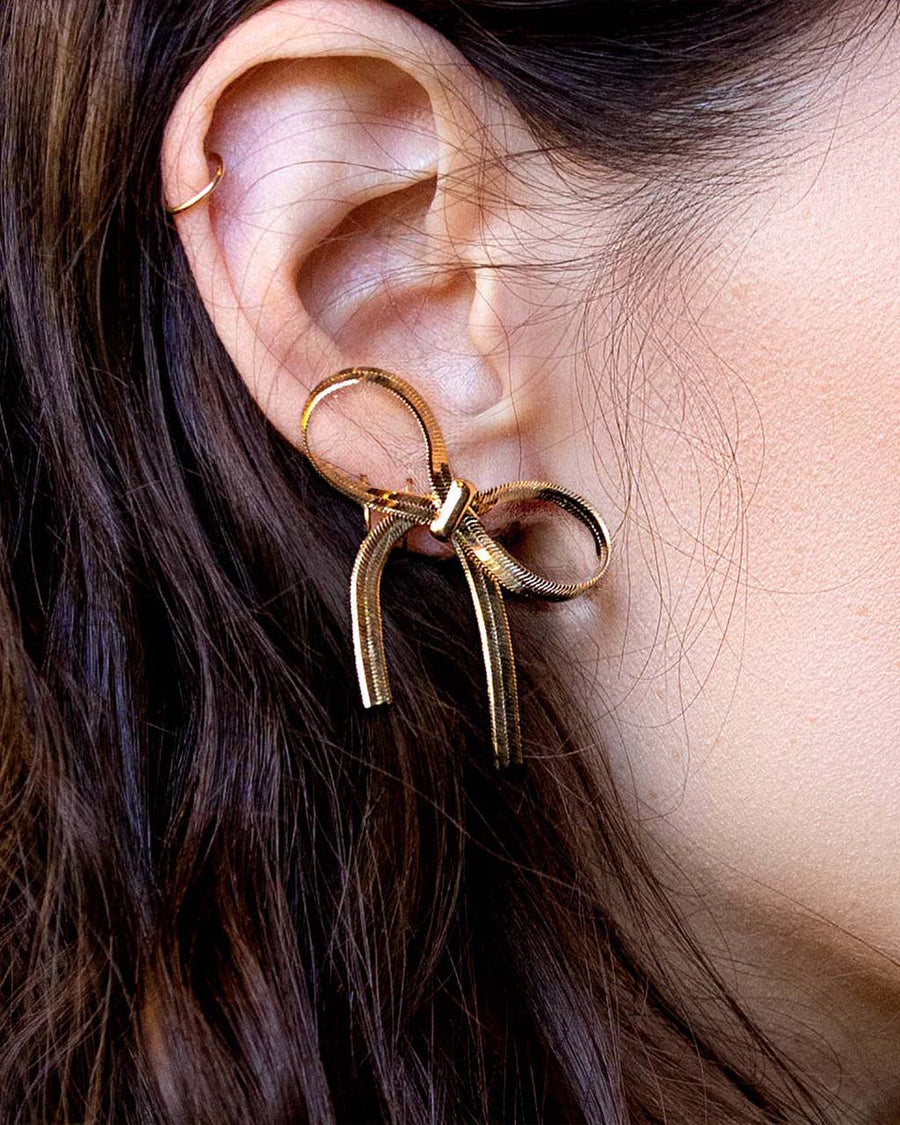 model wearing thick gold bow earrings