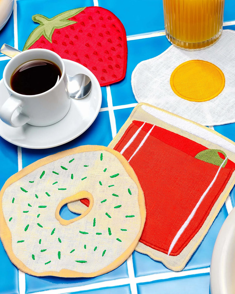 set of 4 brunch linen napkins: bloody mary, strawberry, egg, and bagel with cream cheese in a table setting