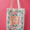 tan canvas bag with orange 'meet me at the library' surrounded by colorful flowers