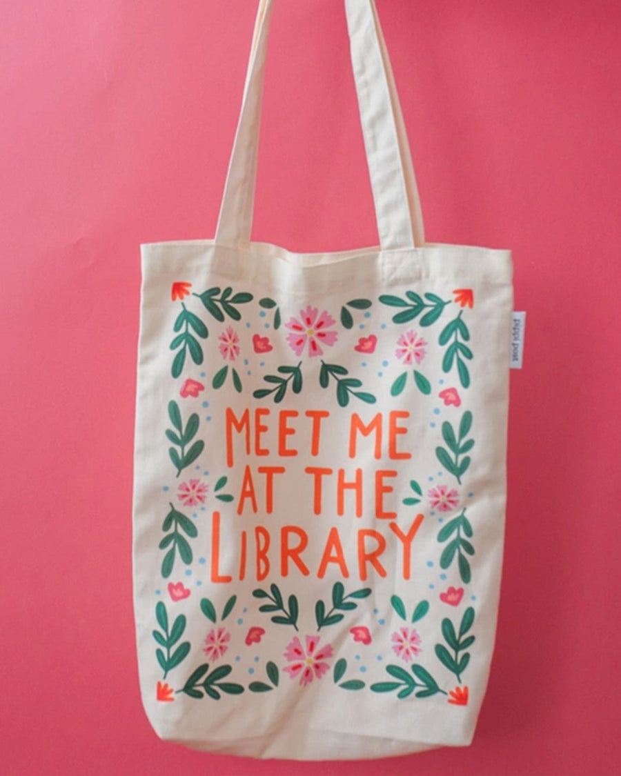 tan canvas bag with orange 'meet me at the library' surrounded by colorful flowers