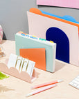 set of three 'forms' desk organizers: blue arch, orange parallelogram, and blush scallop on a desk
