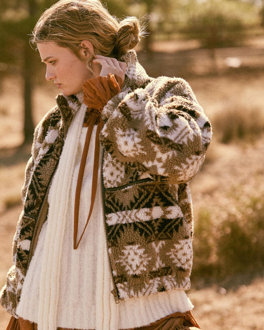 Sideview of model wearing brown and white geometric zip up sherpa sweatshirt with faux leather trim