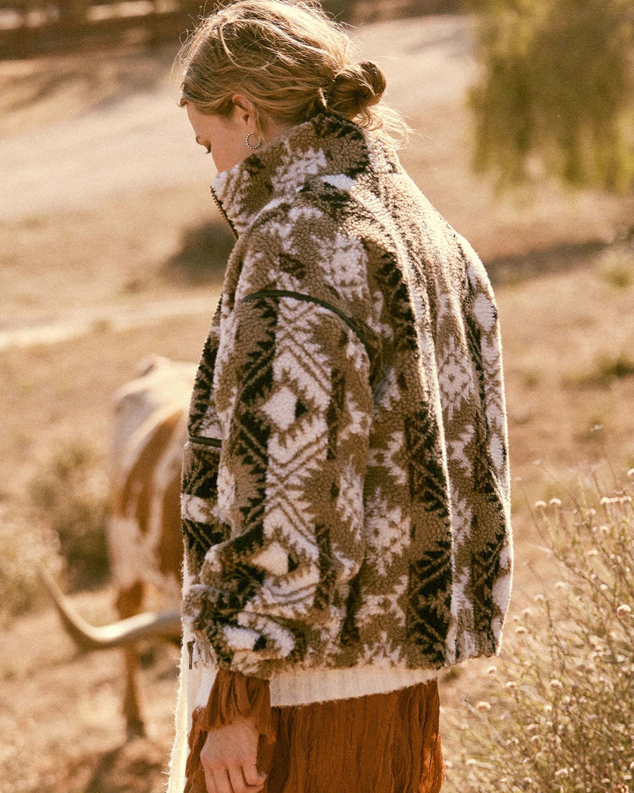 back view of model wearing brown and white geometric zip up sherpa sweatshirt with faux leather trim