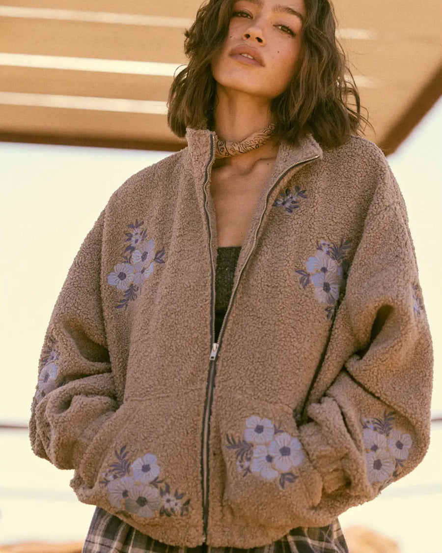 model wearing tan sherpa zip-up jacket with purple embroidered clustered flowers