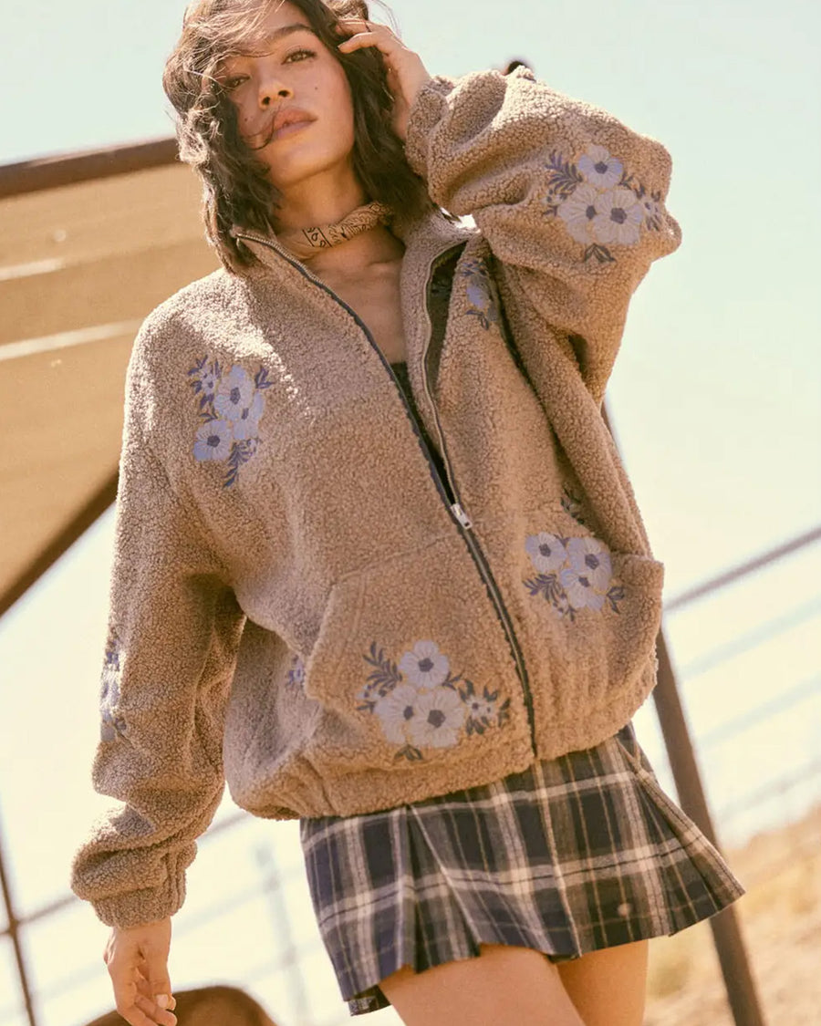 model wearing tan sherpa zip-up jacket with purple embroidered clustered flowers