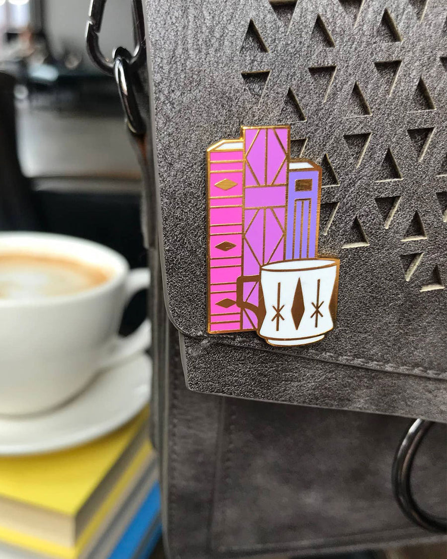 pink and purple geometric books and white mug pin on bag
