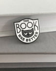 white enamel pin with grey cat and 'the book was better' across the front