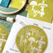 up close of green embroidery kit with cream mushroom design with ring, thread, pre-printed fabric and instructions