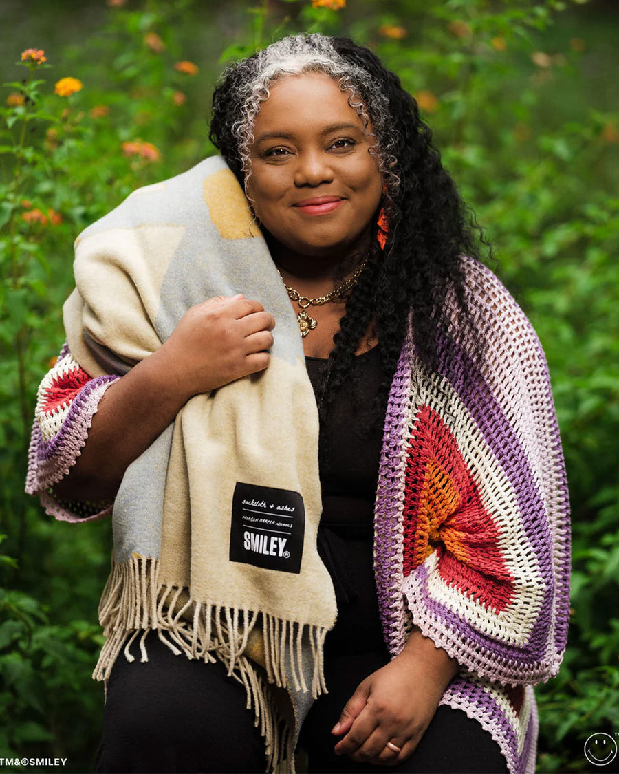 model wearing cream throw blanket with periwinkle flower print with smiley faces in the center