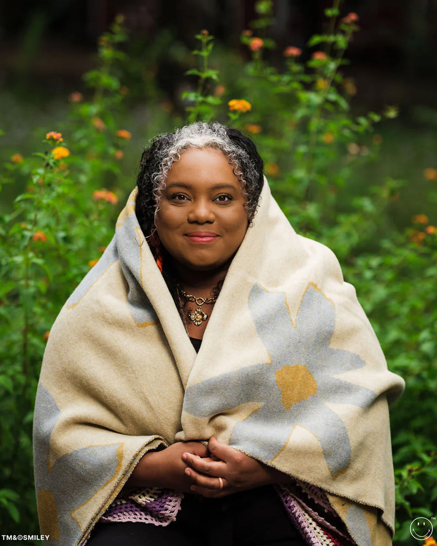 model wrapped in cream throw blanket with periwinkle flower print with smiley faces in the center