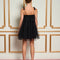 back view of model wearing black tulle tiered mini dress with rosettes on spaghetti straps
