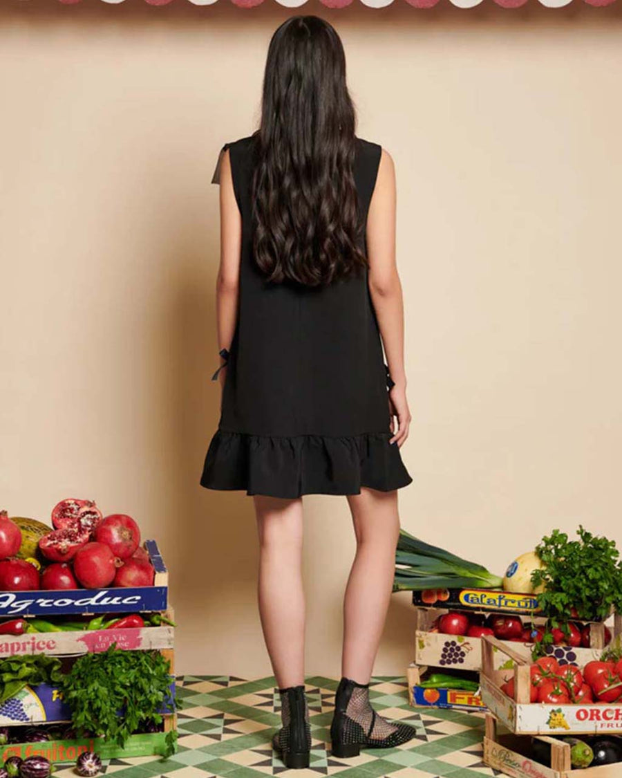 backview of model wearing black mini dress with deep v-neck and bows placed all over