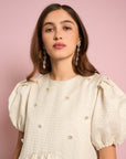 up close of model wearing white textured dress with puff sleeves and flower beading detail