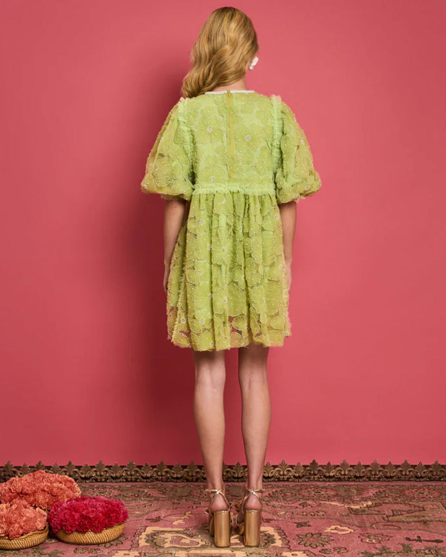 backview of model wearing green tulle mini dress with puff sleeves and embellished flower pattern with pearl neckline