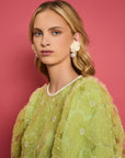 up close of model wearing green tulle mini dress with puff sleeves and embellished flower pattern with pearl neckline