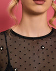 up close of model wearing black sheer long sleeve top with dot texture and pearl beading