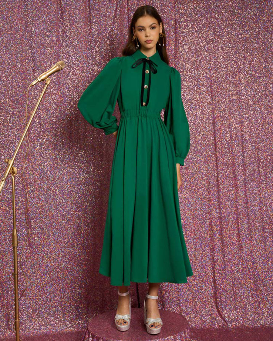 model wearing emerald green midi dress with collar, long puff sleeves, decorative button front and black tie neckline