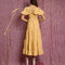 back view of model wearing golden yellow tiered midi dress with puff sleeves, smocked bodice, and back oversized bow