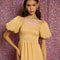 up close of model wearing golden yellow tiered midi dress with puff sleeves, smocked bodice, and back oversized bow