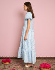 sideview of model wearing light blue tiered midi dress with puff sleeves and subtle pom detail