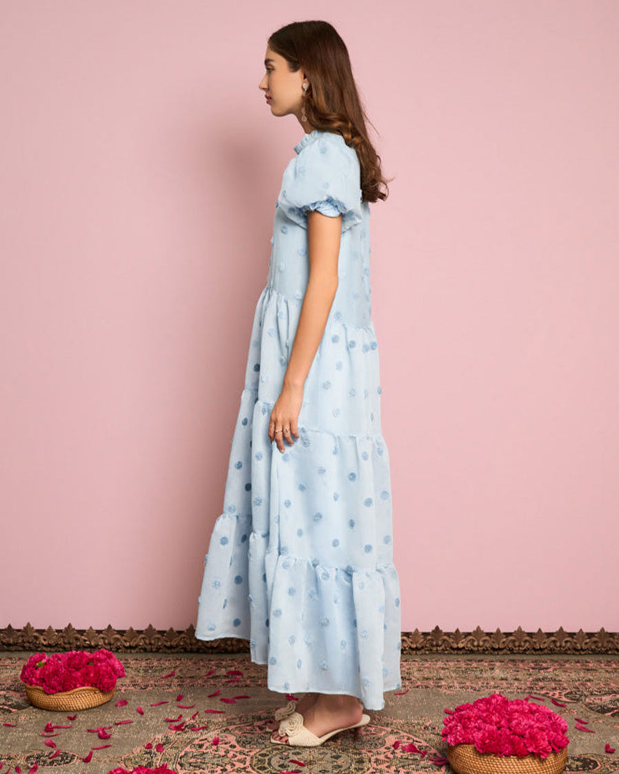sideview of model wearing light blue tiered midi dress with puff sleeves and subtle pom detail
