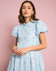 up close model wearing light blue tiered midi dress with puff sleeves and subtle pom detail