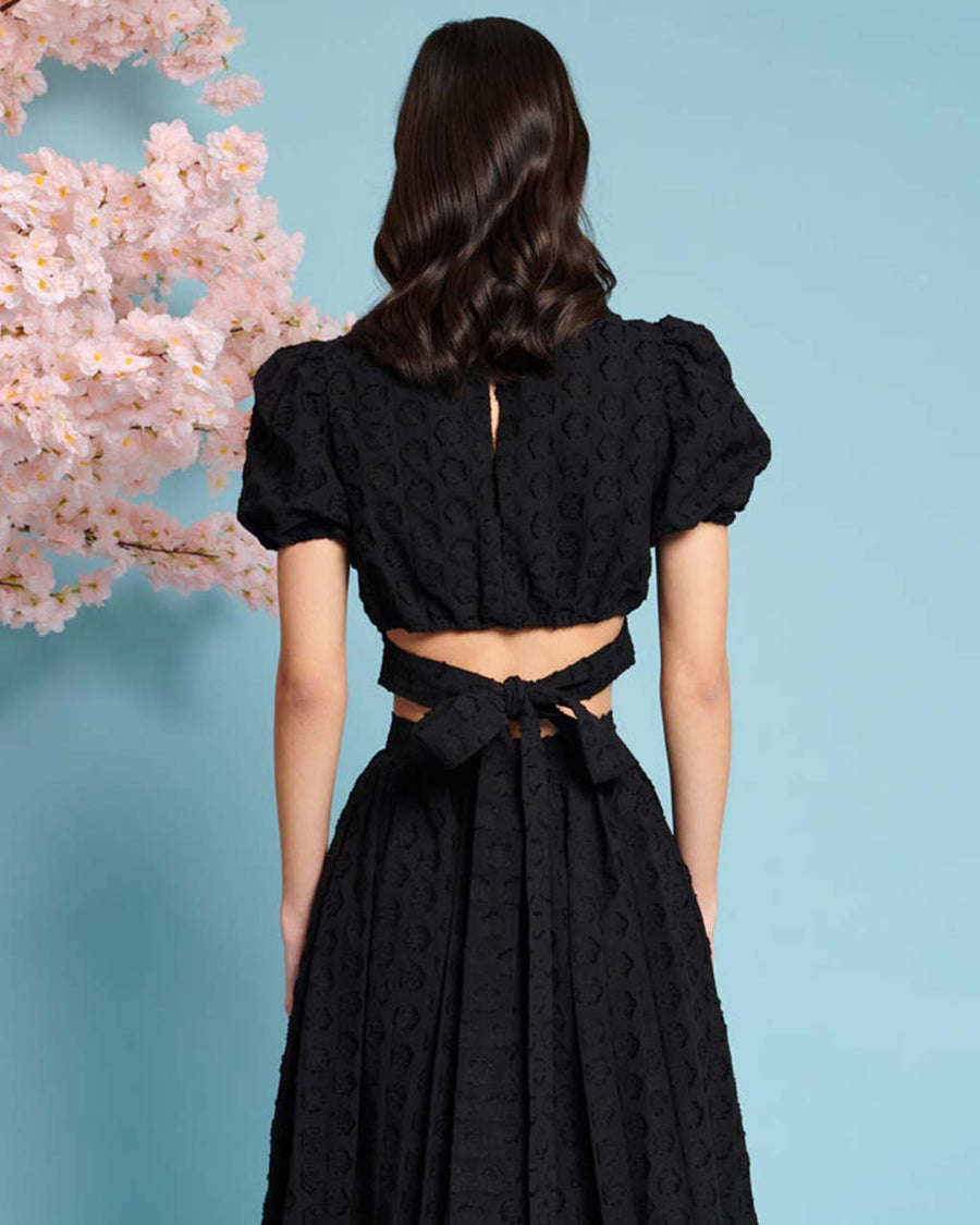 back view of model wearing black jacquard crop top with slight puff short sleeves and tie back