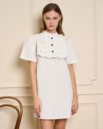 model wearing white mini dress with ruffle bib front with black buttons and short sleeves