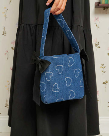 model holding denim blue square handbag with black bows on the sides