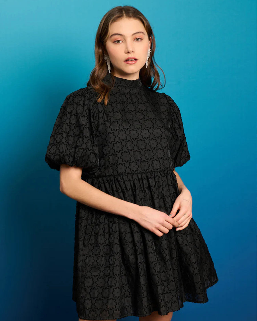 model wearing black textured flower mini dress with mock neck and short puff sleeves