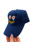 sideview of royal blue baseball cap with smiley with egg eyes and banana mouth