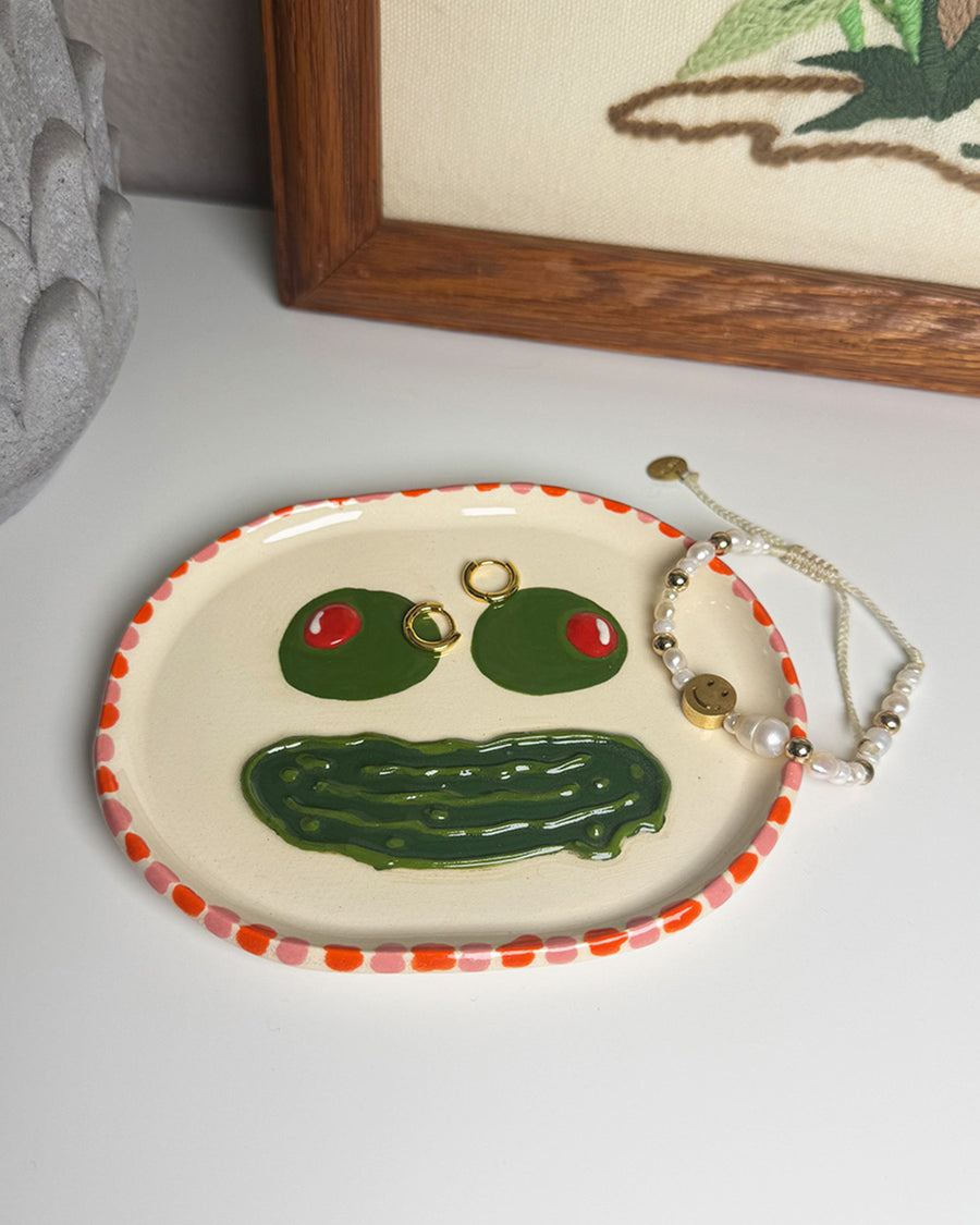 handmade tray with olive eyes and dill pickle smiley face with pink and red trim with jewelry on it