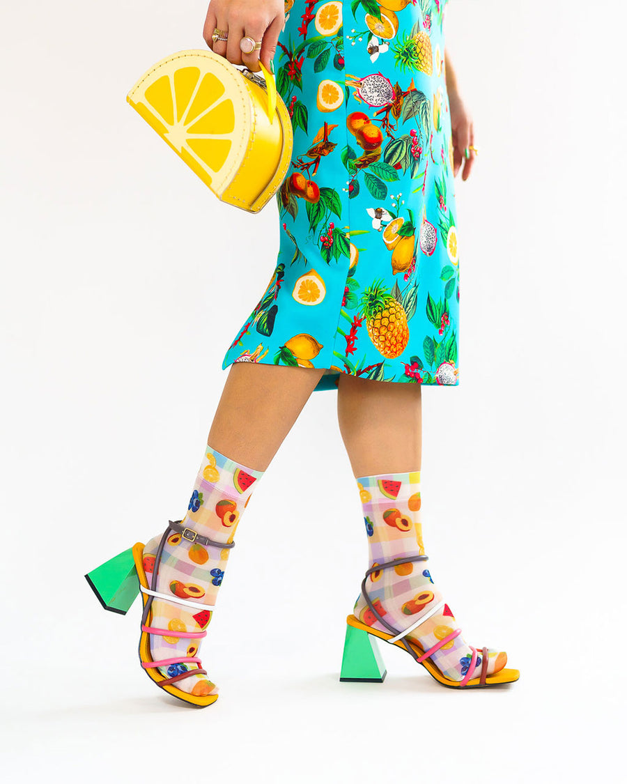 side view of model wearing colorful plaid socks with all over fruit print