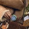 model placing blue and gold pill compact with a cross-stitch DRUGS and vine border in their purse