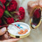 model placing pills inside of blue and gold pill compact with a cross-stitch DRUGS and vine border