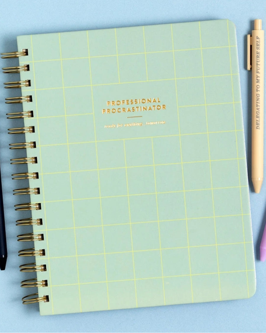green grid notebook with gold foil 'professional procrastinator' across the front on a blue background