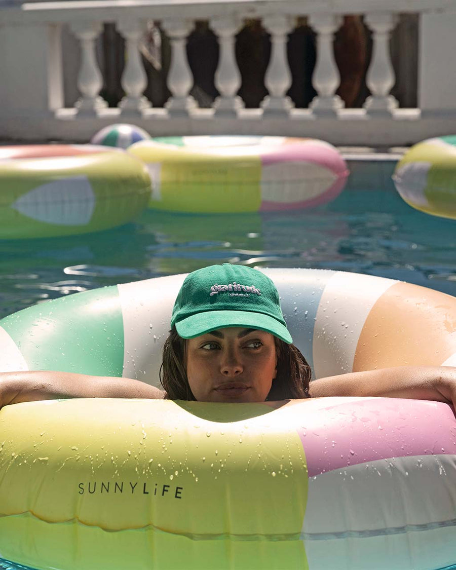 model floating on cream pool ring with pastel green, blue, orange and pink sun beams