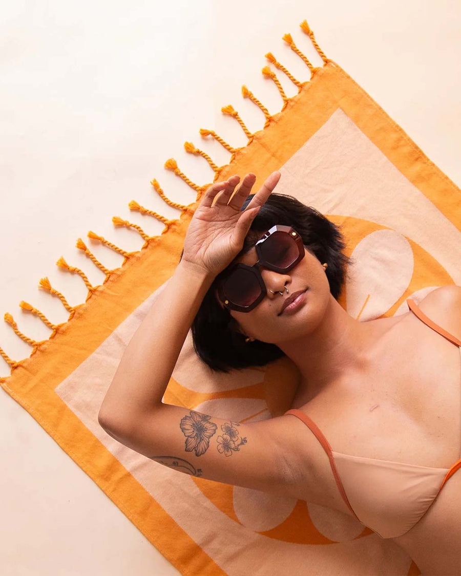 model laying on orange and white retro flower towel with tassels on the end
