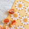 yellow kitchen towel with white 70's inspired flower print with fruit laying on it