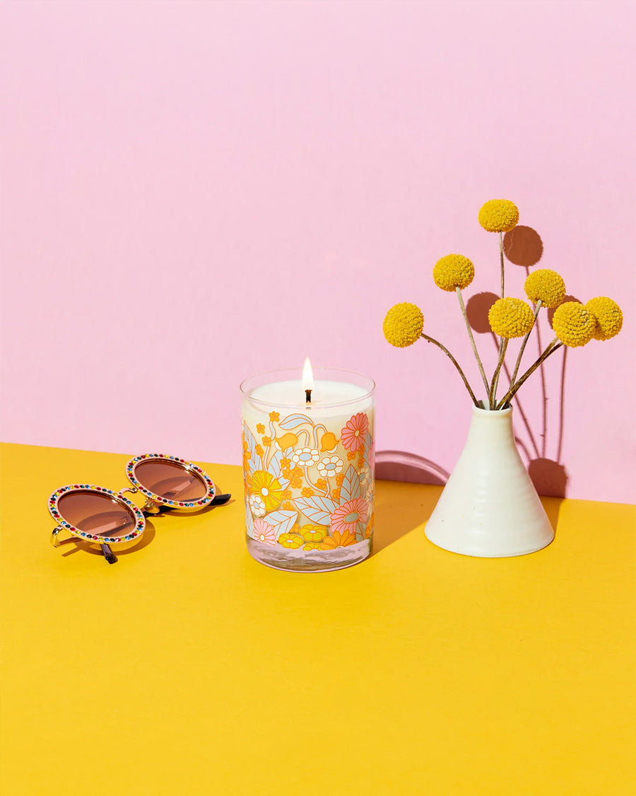 glass candle with vibrant abstract floral print with a vase of flowers and sunglasses