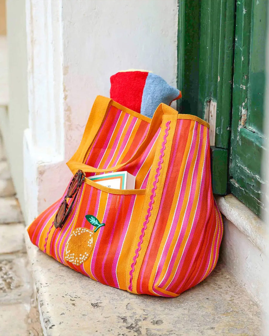 orange, yellow, and pink vertical stripe recycled plastic tote with ribbon detail and lemon applique on a step