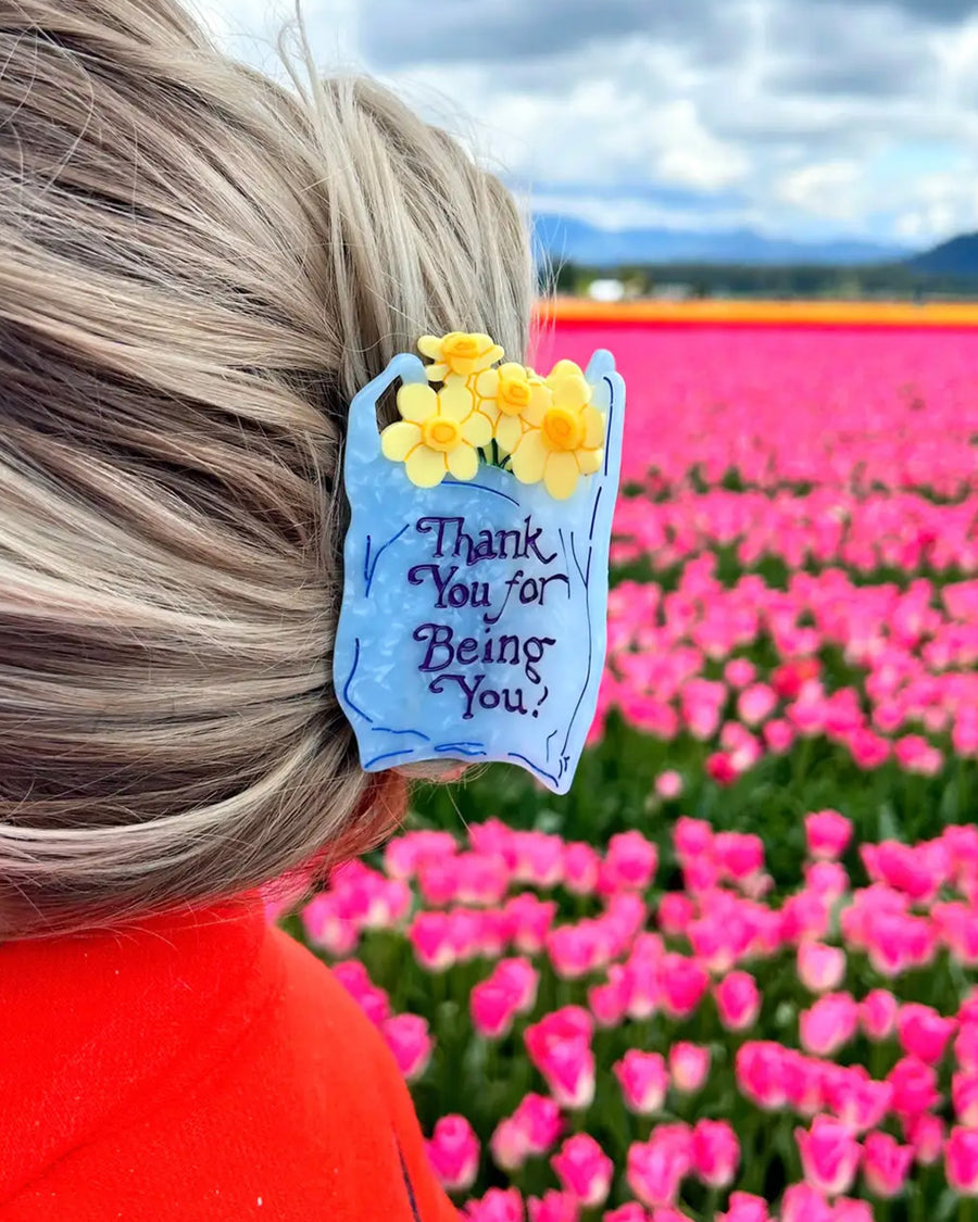 model wearing light blue 'plastic bag' hair claw with 'thank you for being you' across the front and yellow daffodils coming from the top