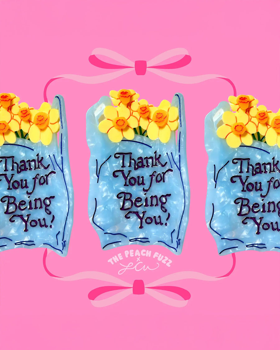 up close of light blue 'plastic bag' hair claw with 'thank you for being you' across the front and yellow daffodils coming from the top