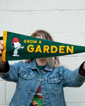 model holding green pennant flag with snoopy graphic and gold trim and 'grow a garden' typography