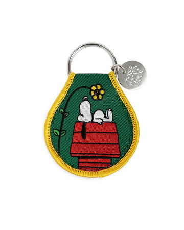 dark green patch keychain with snoopy on his doghouse looking up at a flower
