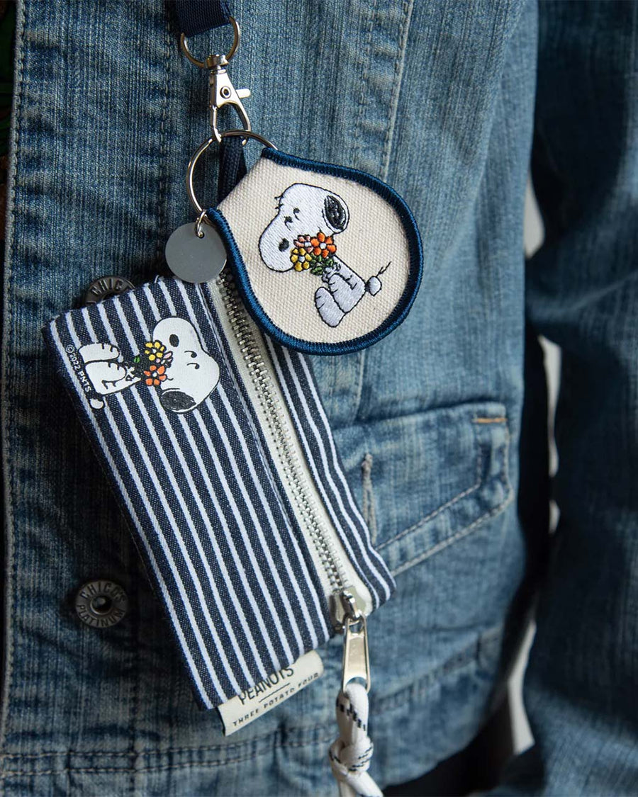 model wearing tan patch keychain with snoopy holding a bouquet of flowers and navy blue trim