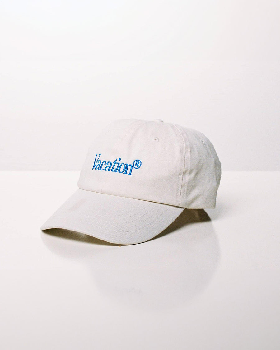 white baseball cap with blue embroidered 'vacation' across the front