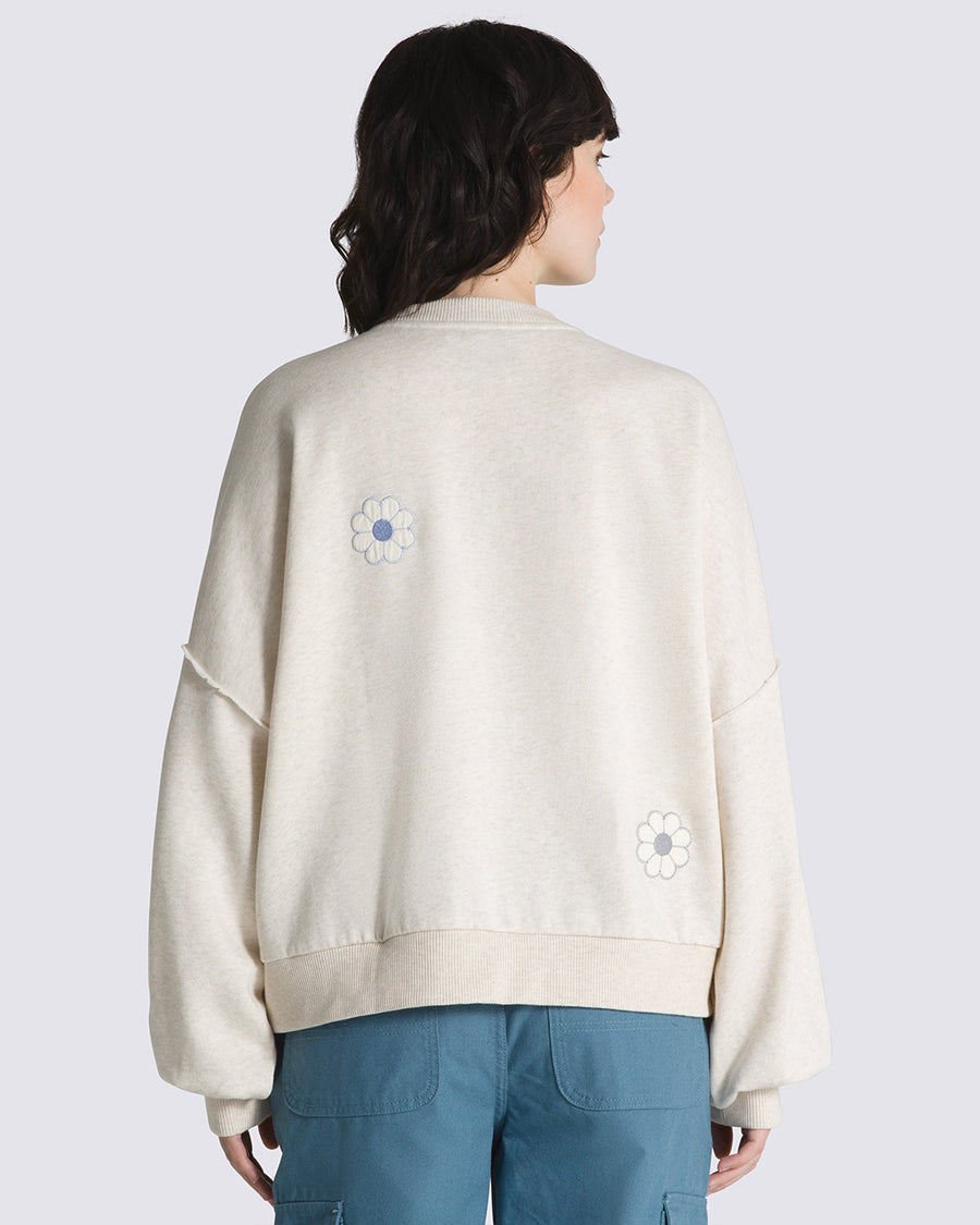 backview of model wearing cream sweatshirt with all over blue flower appliques, blousant sleeves, and black vans logo