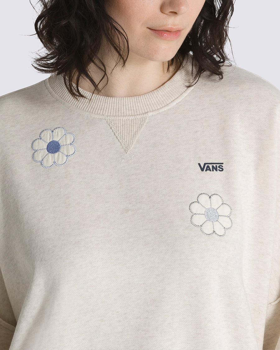 up close of model wearing cream sweatshirt with all over blue flower appliques, blousant sleeves, and black vans logo
